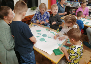 Dzieci wraz z rodzicami ozdabiają choinkę