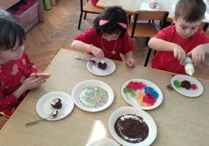 Dzieci dekorują kremem, posypką i galaretkami muffinki.