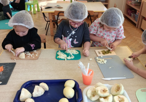 Trzy dziewczynki kroją seler, pietruszkę i ogórka.