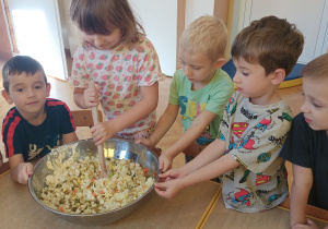 Dziewczynka miesza sałatkę, a chłopcy trzymają miskę.