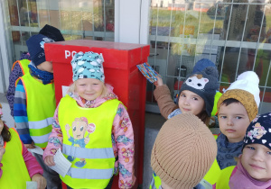 Dziewczynka wrzuca widokówkę do skrzynki pocztowej.