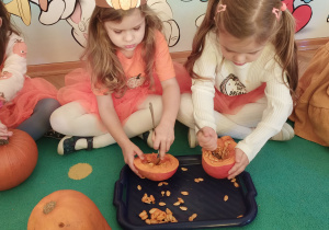 Dwie dziewczynki wydrążają miąższ z dyni.