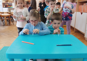 Chłopiec z dziewczynką dmuchają przez słomki na kredki.