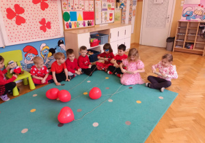 4 dzieci przyciąga balonowe serduszka, nawijając sznurek na rolkę.
