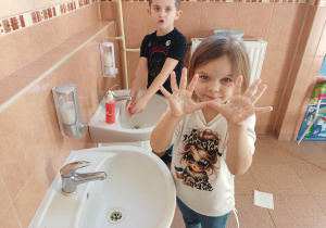 Dziewczynka pokazuje namydlone ręce.