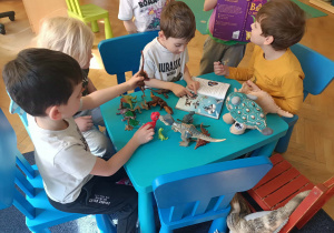 Dzieci bawią się dinozaurami i oglądają książkę.