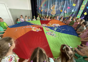 Dzieci poruszają chustą animacyjną z kolorowymi kwiatkami.