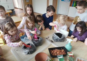 Dziewczynki sypią ziemię do doniczek.