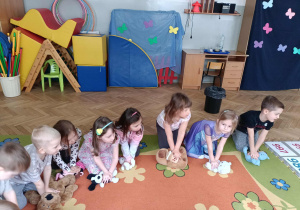 Dzieci wykonują uciski na klatkę piersiową przytulanek.