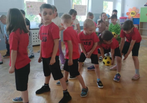 Dzieci przekazują sobie piłkę pod nogami.