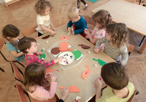 Dzieci tworzą przy stoliku dinozaury, z gotowych elementów.