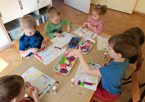 Dzieci wyklejają sztućce kolorowym papierem wycinankowym.