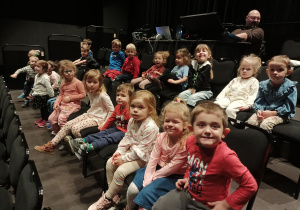 Dzieci siedzą na widowni i oczekują na spektakl.