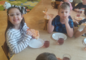 Dzieci zadowolone jedzą pizzę.