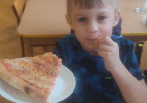 Chłopiec trzyma w ręku pizzę i pokazuje jak mu smakuje.