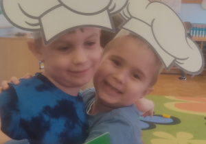 Dwóch chłopców przytula się do siebie, obaj mają na głowie czapkę kucharza.