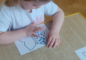 Dziewczynka palcem maluje motyla.