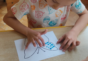 Chłopiec palcem maluje motyla.