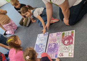Dzieci z Panem Tomkiem układają banknoty od najmniejszego do największego nominału.