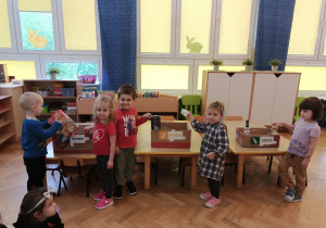 Dzieci segregują śmieci do trzech pudełek oznaczonych na żółto, niebiesko i zielono.