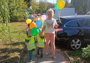 Nauczycielka i dzieci idą z balonami po osiedlu.