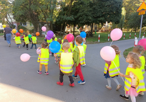 Dzieci z balonami mijają kolejne bloki mieszkalne.